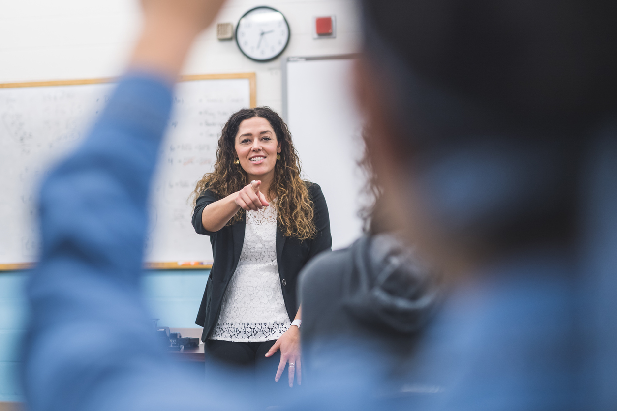 female teacher pointing at individual with raised hand